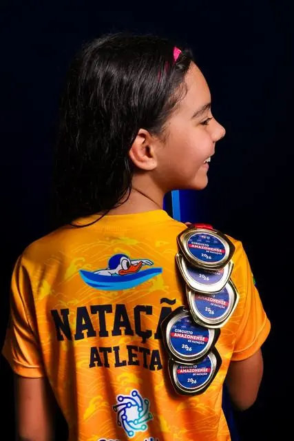 Lelê de costas, com a camisa Natação Atleta e várias medalhas no ombro