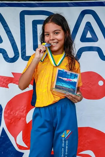 Lelê mordendo a medalha diante de um painel colorido